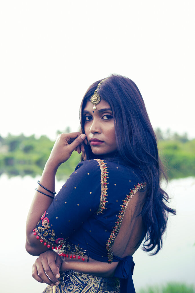 Woman in a navy embroidered blouse looking back over her shoulder beside still water