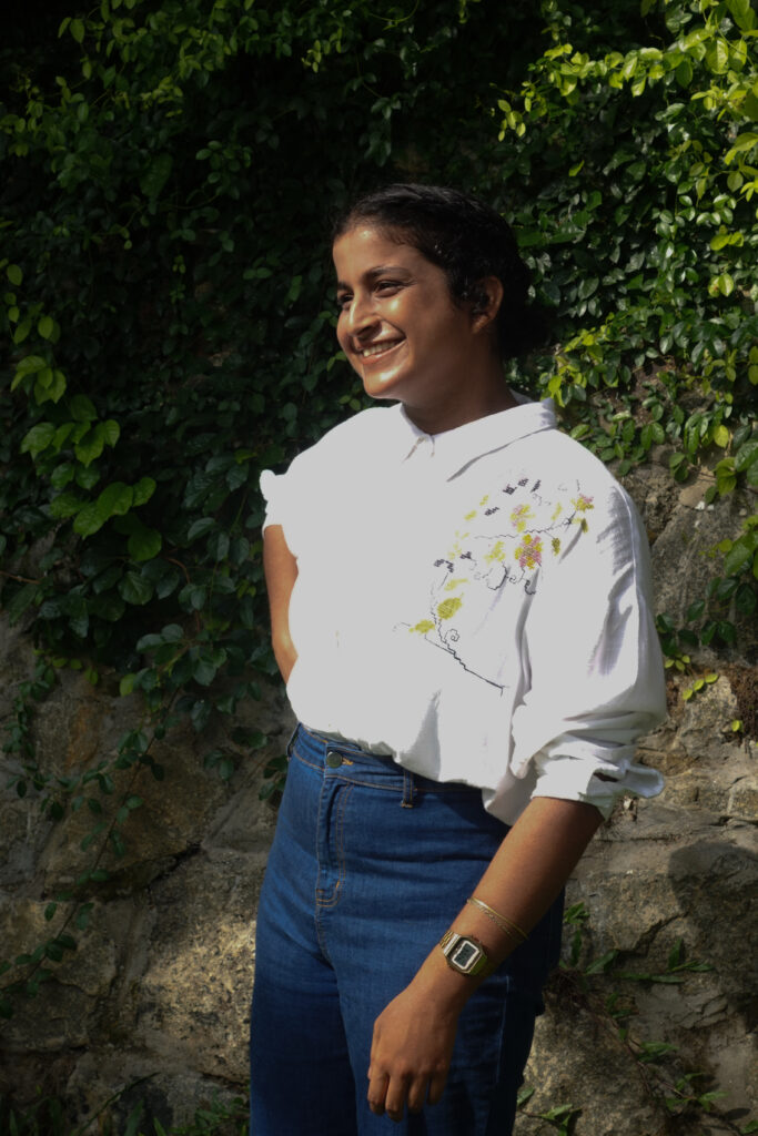 Smiling woman in a white shirt and jeans against an ivy wall