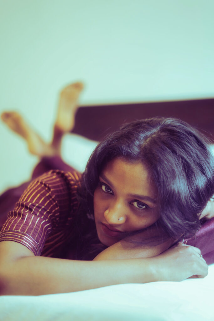 Woman lying on a bed resting her chin on her arms against a mint wall