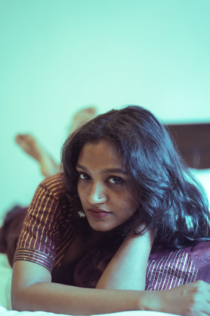 Woman lying on a bed resting her chin on her arms against a mint green wall