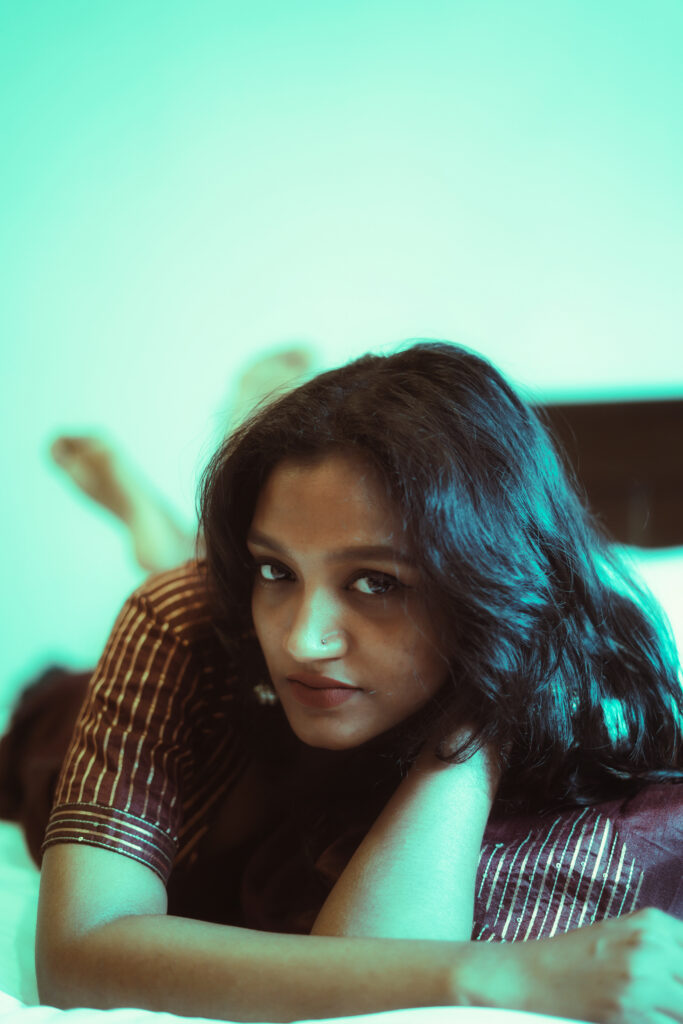 Woman lying on a bed resting her chin on her arms against a mint wall