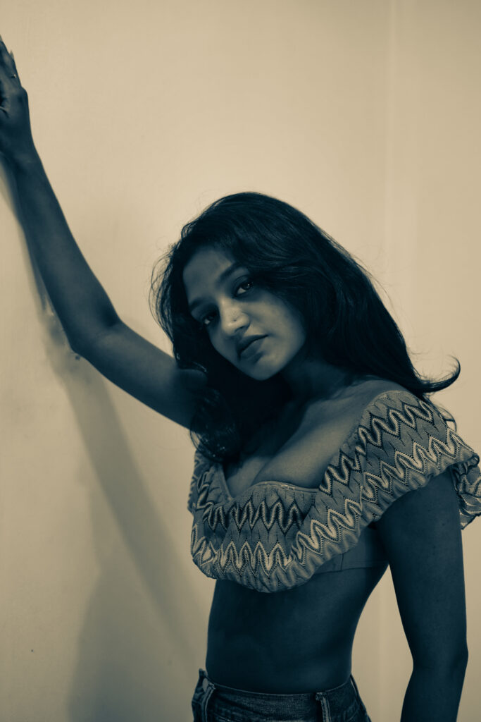Monochrome editorial portrait of a woman in a patterned top against a wall