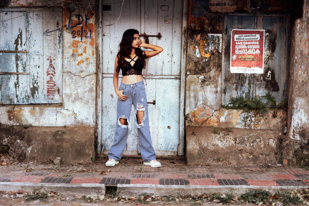 Woman in ripped jeans posing in front of a weathered old shop door