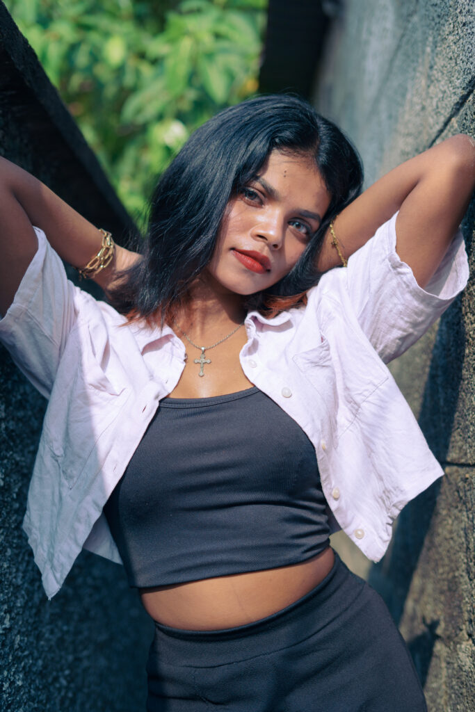 Woman in an open pink shirt and black top posing among green plants