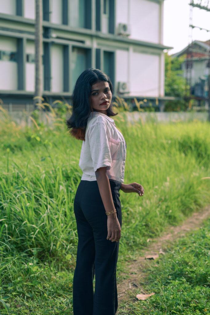 Woman in an open pink shirt and black top posing among green plants
