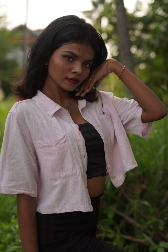 Woman in an open pink shirt and black top posing among green plants