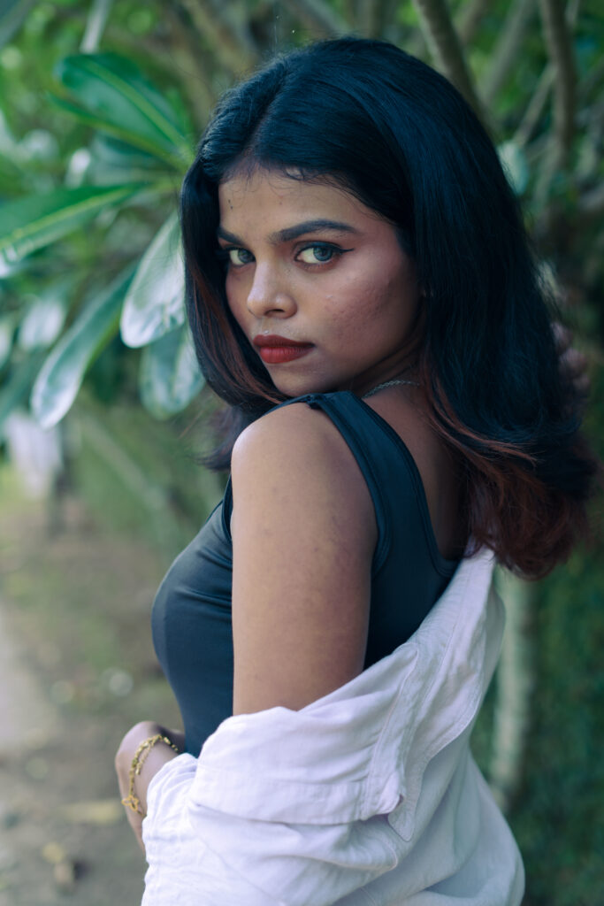 Woman in an open pink shirt and black top posing among green plants