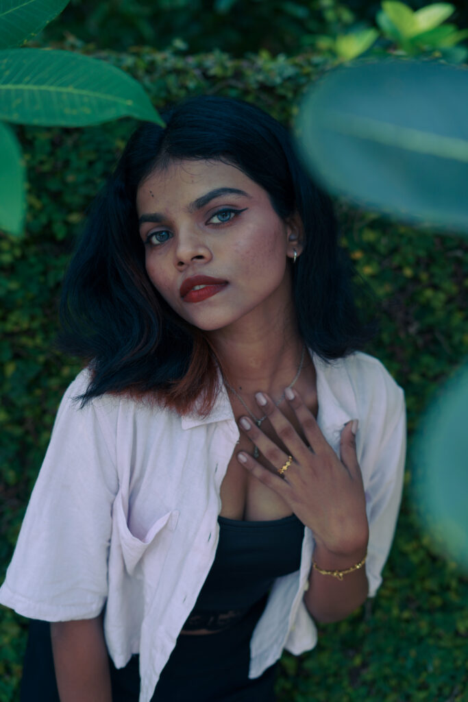 Woman in an open pink shirt and black top posing among green plants