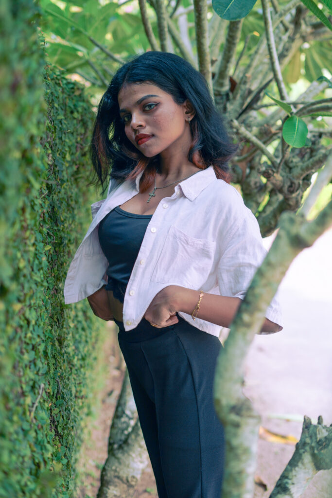 Woman in an open pink shirt and black top posing among green plants