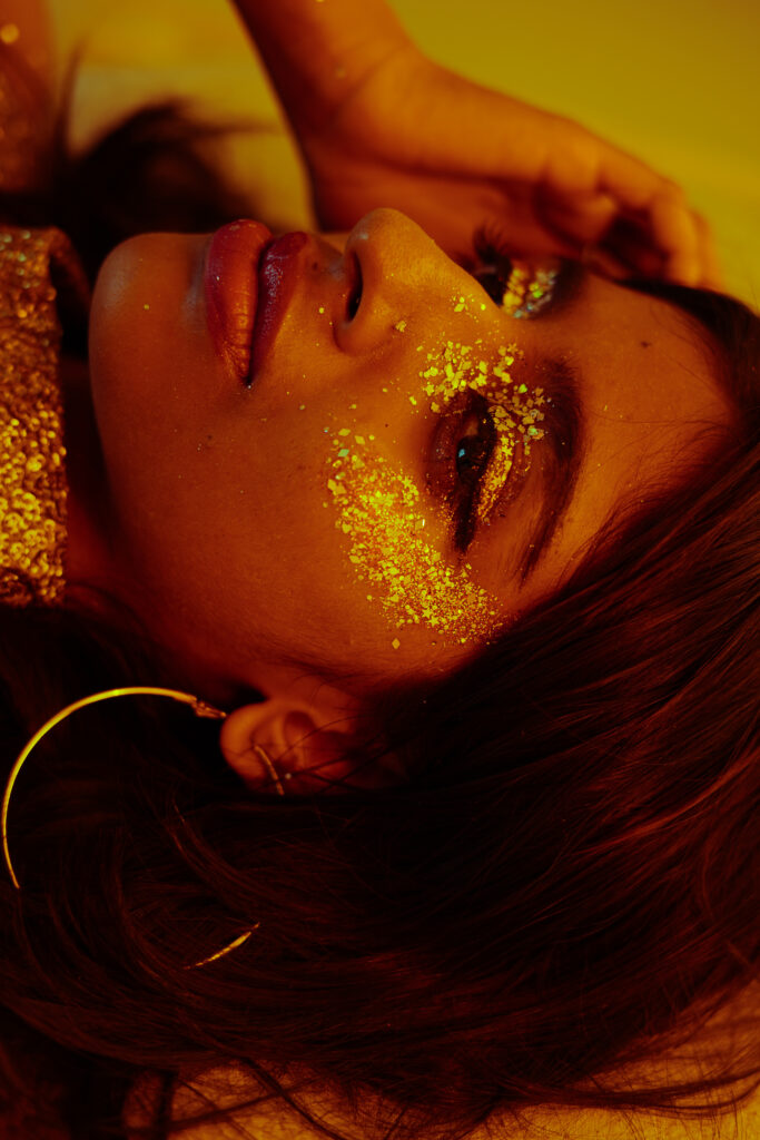 Editorial portrait of a woman with gold glitter on her face and body