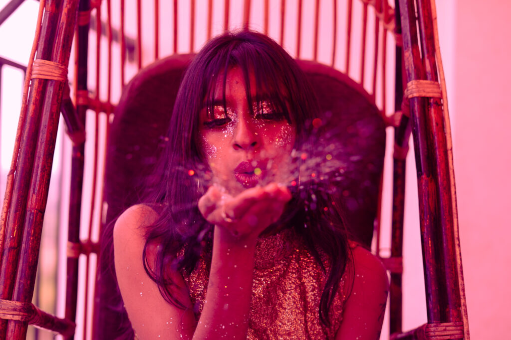 Woman blowing glitter towards the camera in saturated pink light