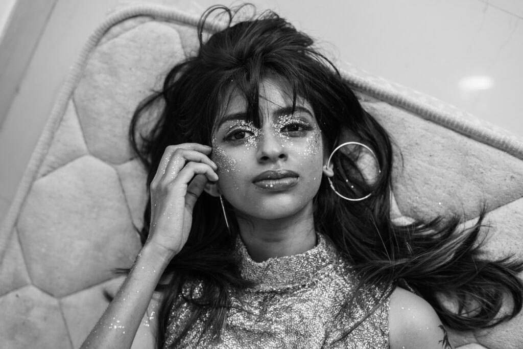 Black and white portrait of a woman lying down wearing hoop earrings, hands framing her face