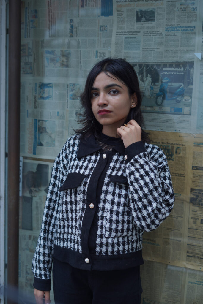 Woman in a houndstooth jacket posing against a newspaper-covered wall
