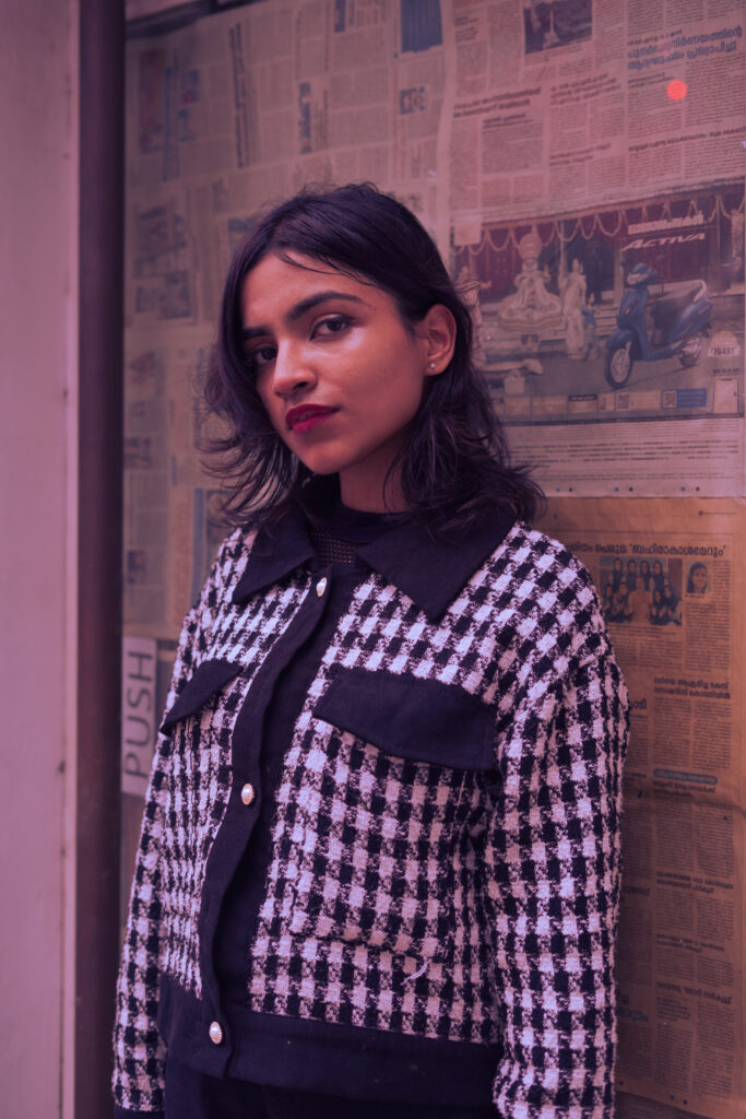 Woman in a houndstooth jacket against a wall of old newspapers in pink light