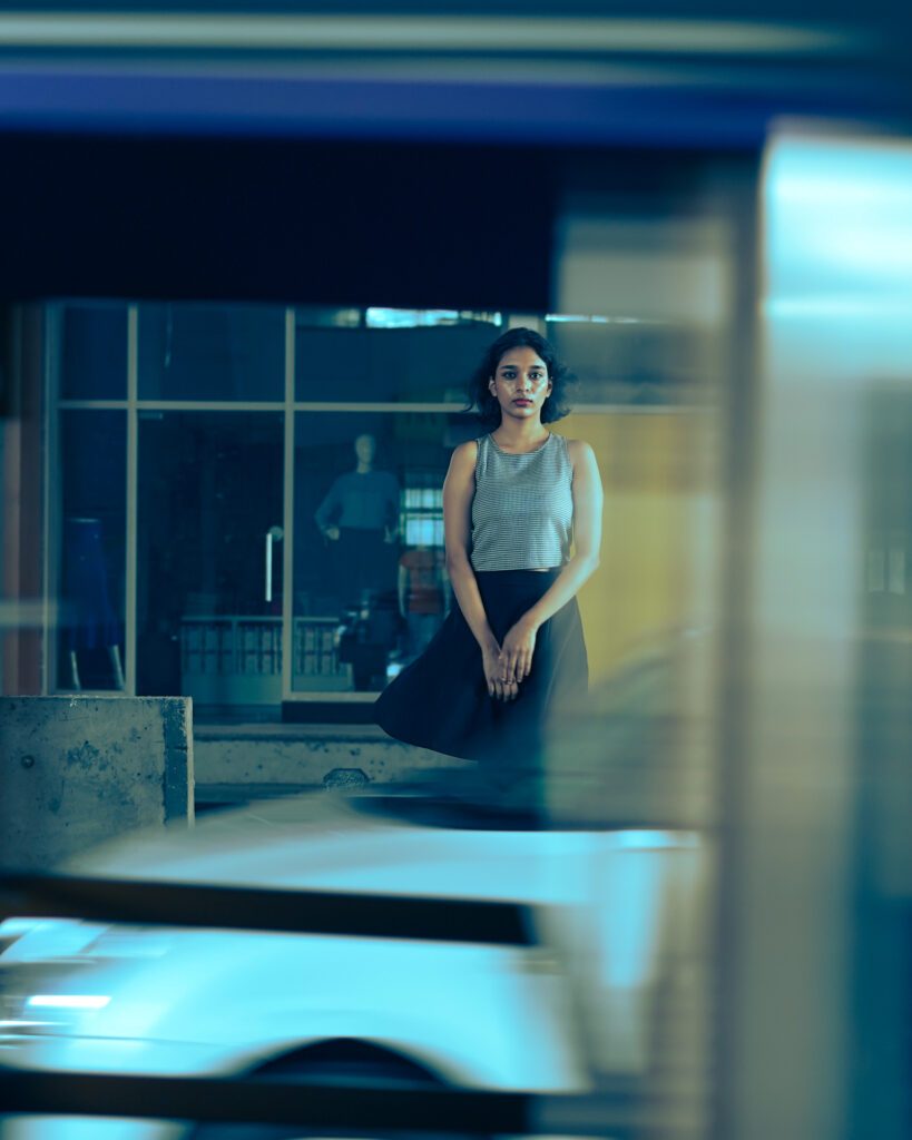 Woman standing among layered glass reflections in cool blue city light
