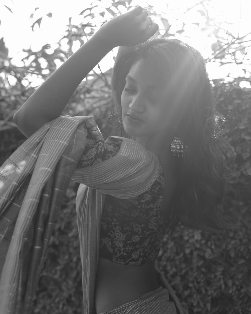 Black and white portrait of a woman in a saree with light falling through branches