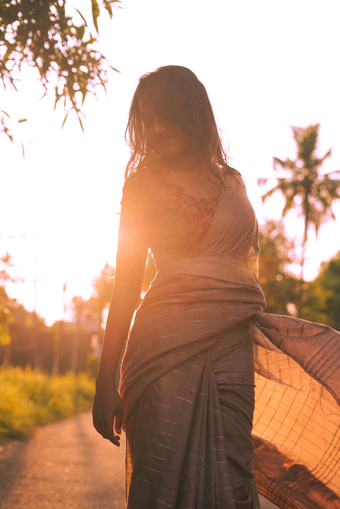Backlit woman in a flowing saree on a path at sunset, coconut palms behind