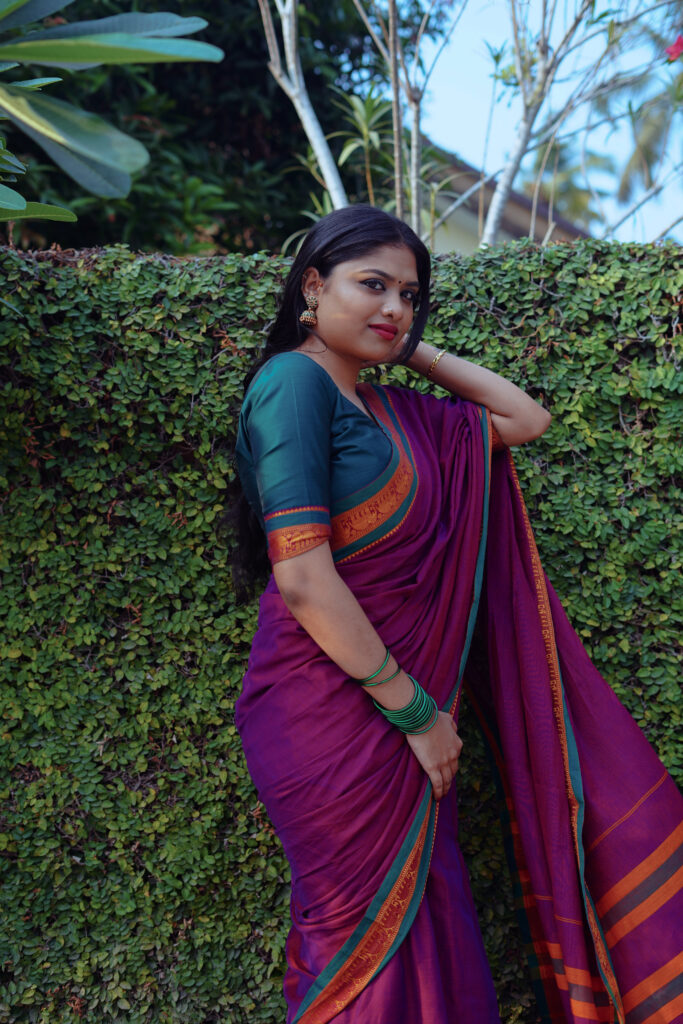 Woman in a magenta silk saree with a green blouse among plants and flowers