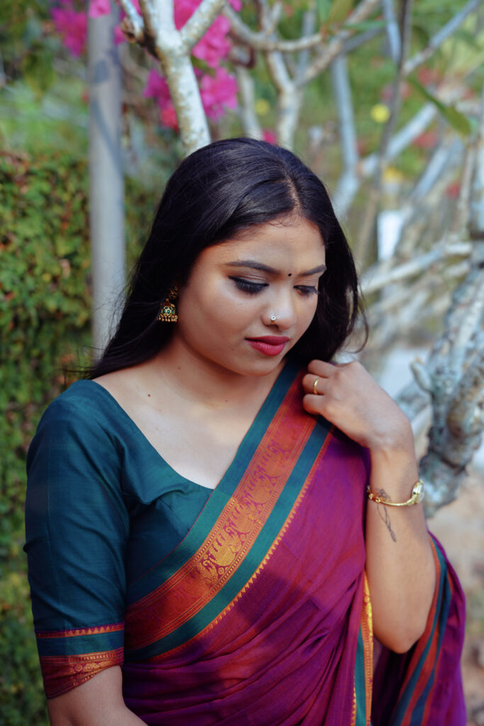 Woman in a magenta silk saree with a green blouse among plants and flowers