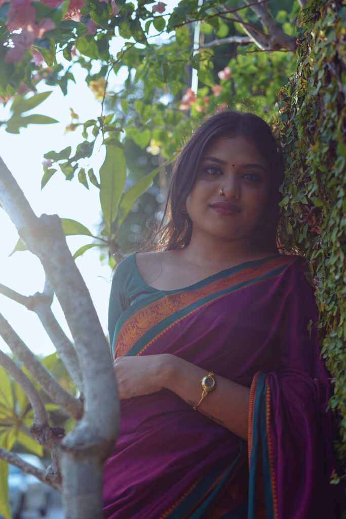 Woman in a magenta silk saree with a green blouse among plants and flowers