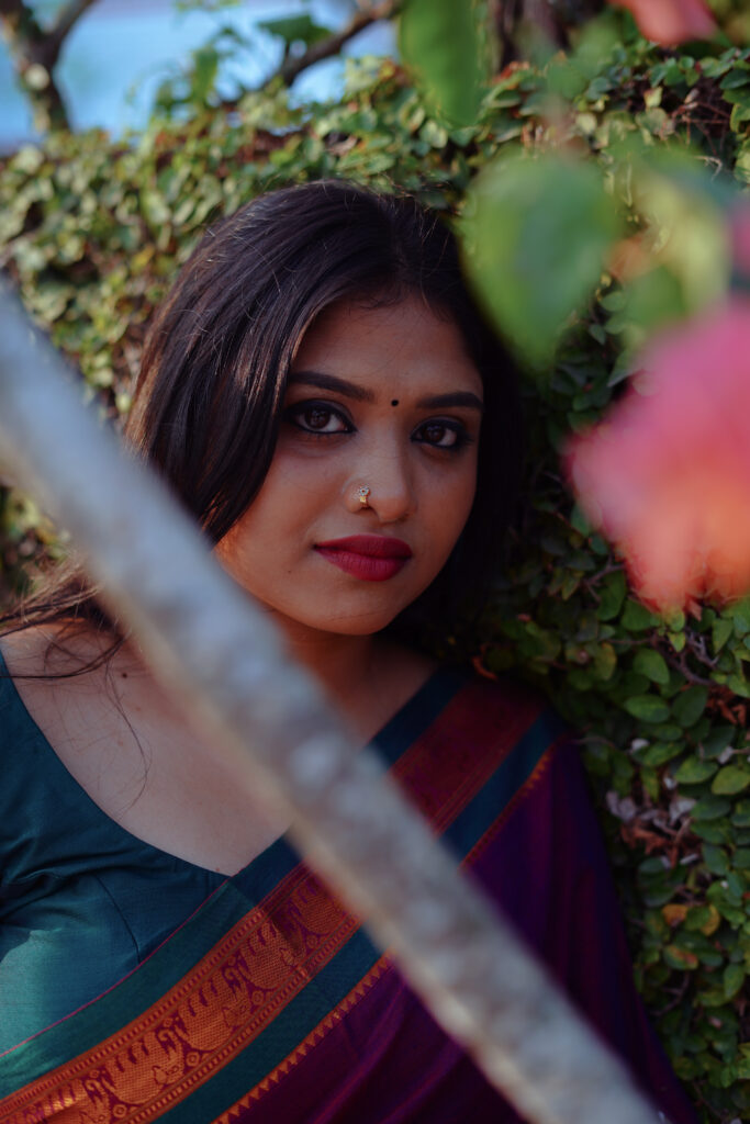 Woman in a magenta silk saree with a green blouse among plants and flowers