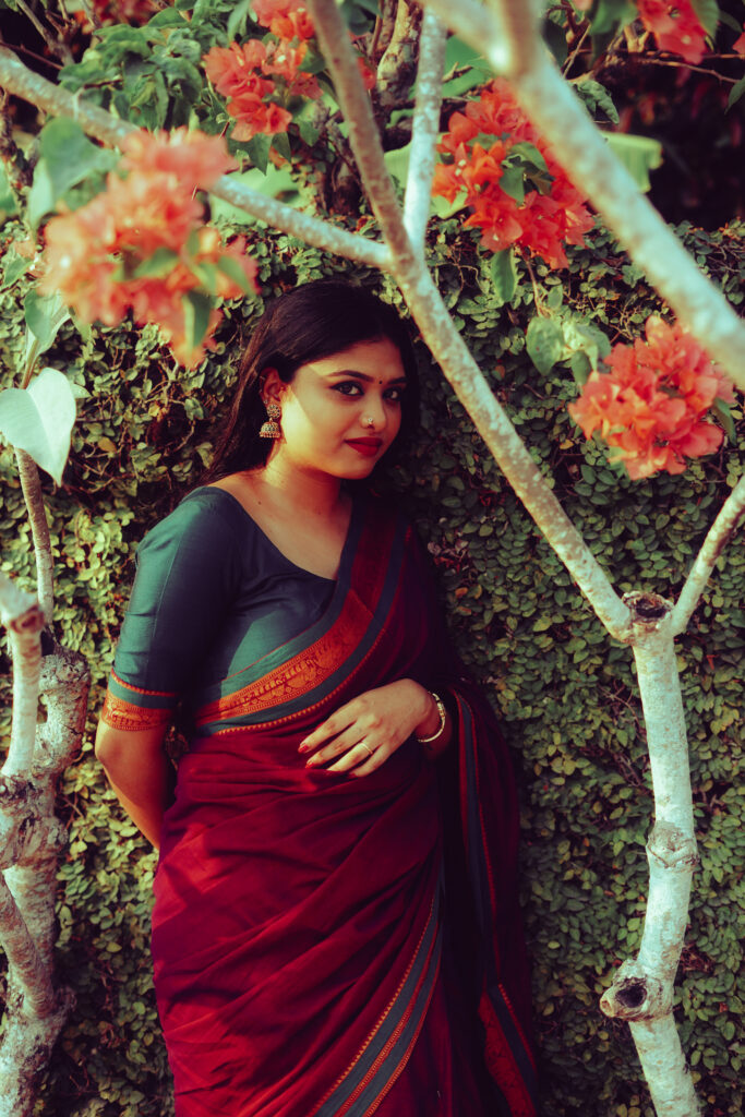 Woman in a magenta silk saree with a green blouse among plants and flowers