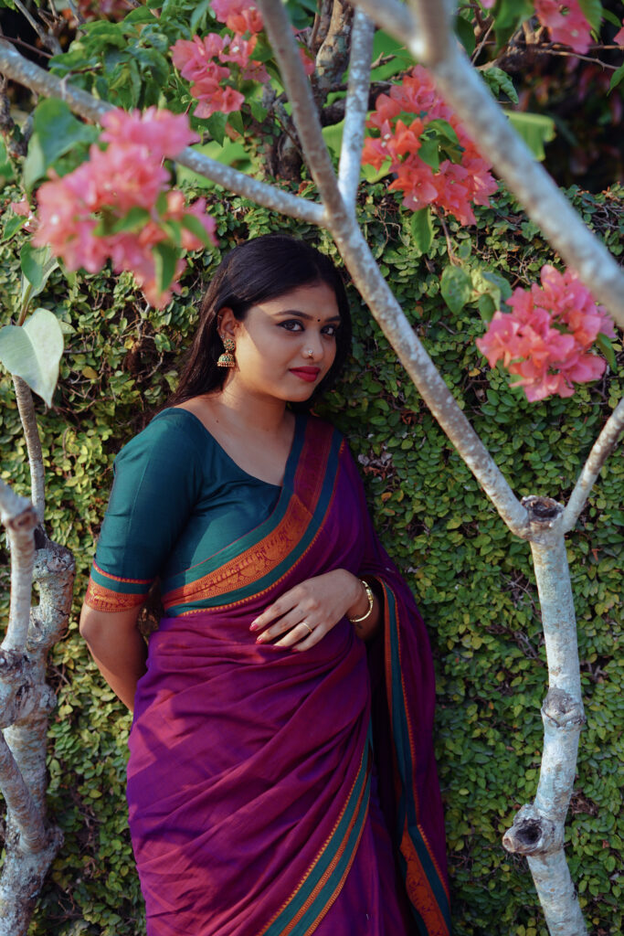 Woman in a magenta silk saree with a green blouse among plants and flowers