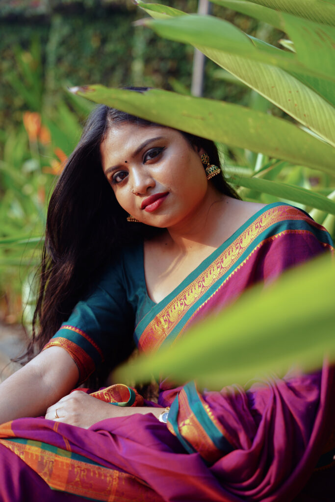 Woman in a magenta silk saree with a green blouse among plants and flowers