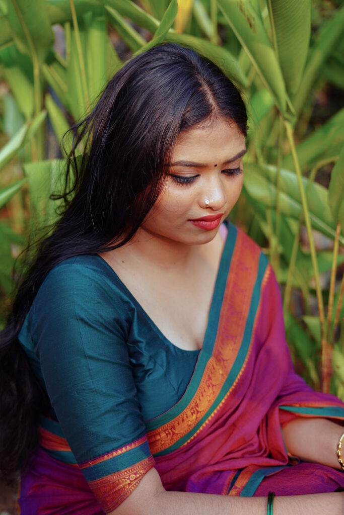 Woman in a magenta silk saree with a green blouse among plants and flowers