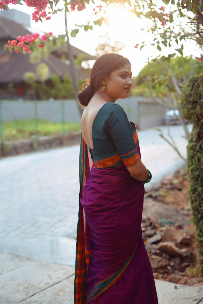Woman in a magenta silk saree with a green blouse among plants and flowers