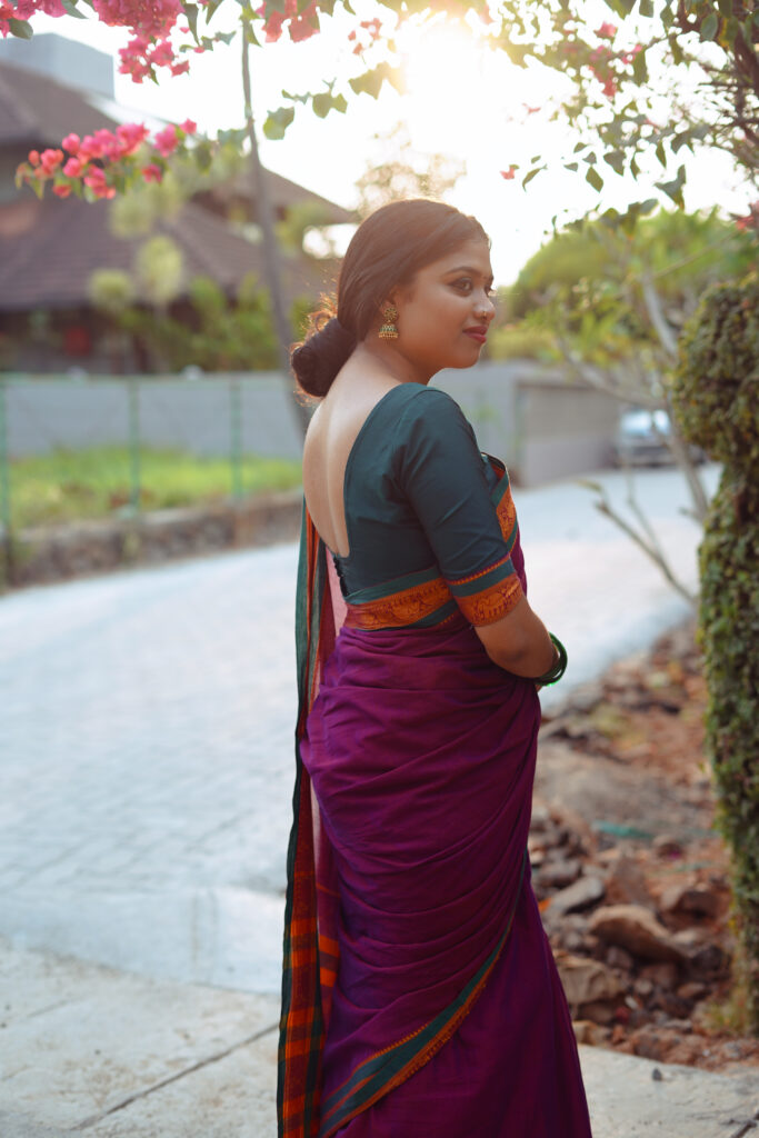 Woman in a magenta silk saree with a green blouse among plants and flowers