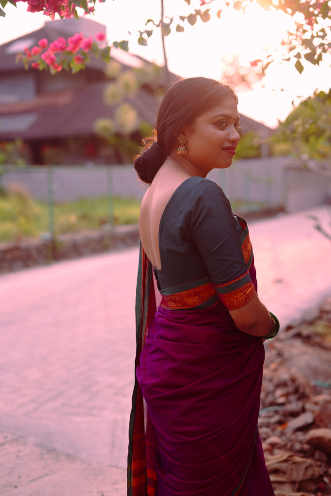 Woman in a magenta silk saree with a green blouse among plants and flowers