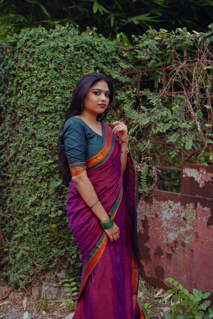 Woman in a magenta silk saree with a green blouse among plants and flowers