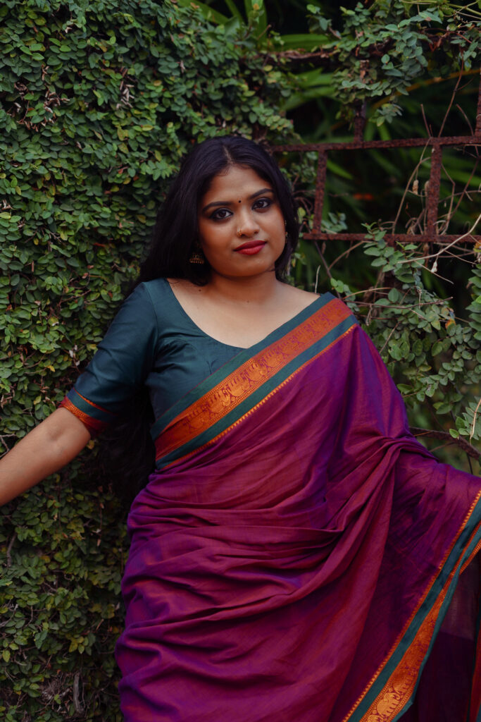 Woman in a magenta silk saree with a green blouse against an ivy-covered wall
