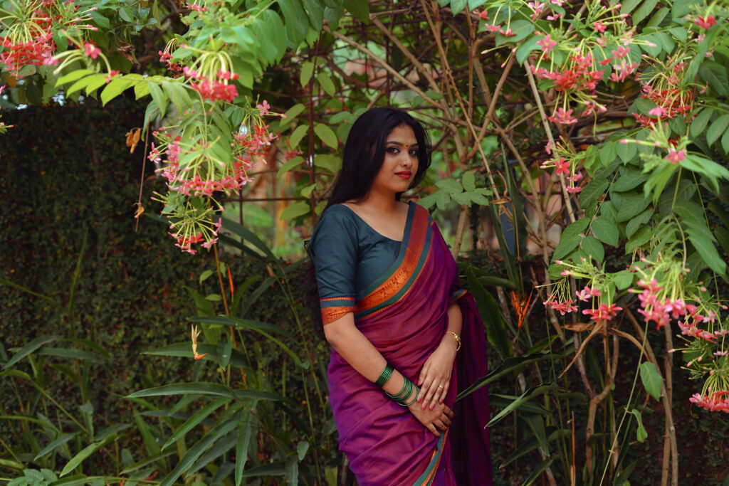 Woman in a magenta silk saree with a green blouse among plants and flowers