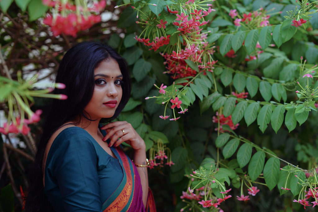 Woman in a magenta silk saree with a green blouse among plants and flowers
