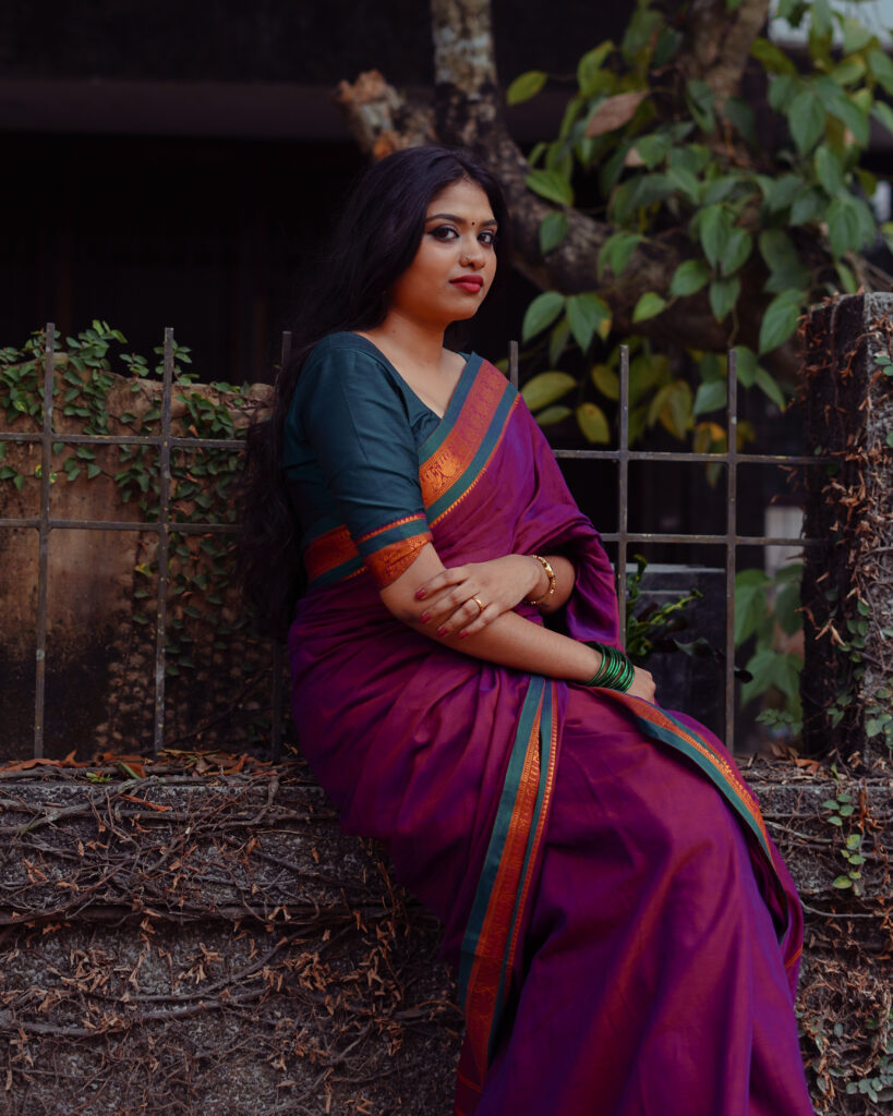 Woman in a magenta silk saree with a green blouse among plants and flowers