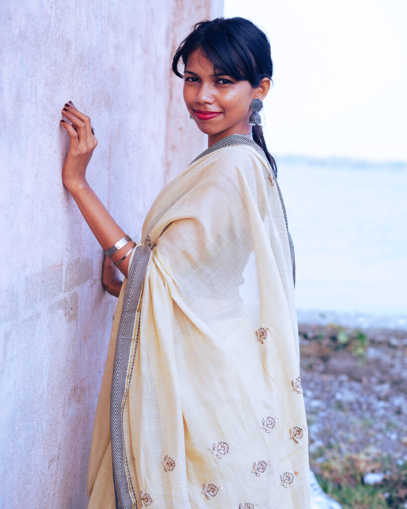 Woman in a cream saree and black blouse by the river, wind in her hair