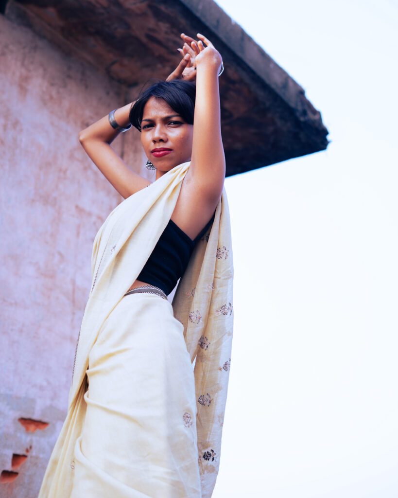Woman in a cream saree and black blouse by the river, wind in her hair