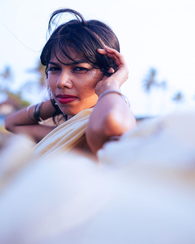 Woman in a cream saree and black blouse by the river, wind in her hair