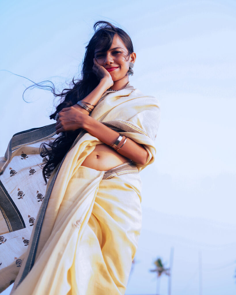 Woman in a cream saree and black blouse by the river, wind in her hair