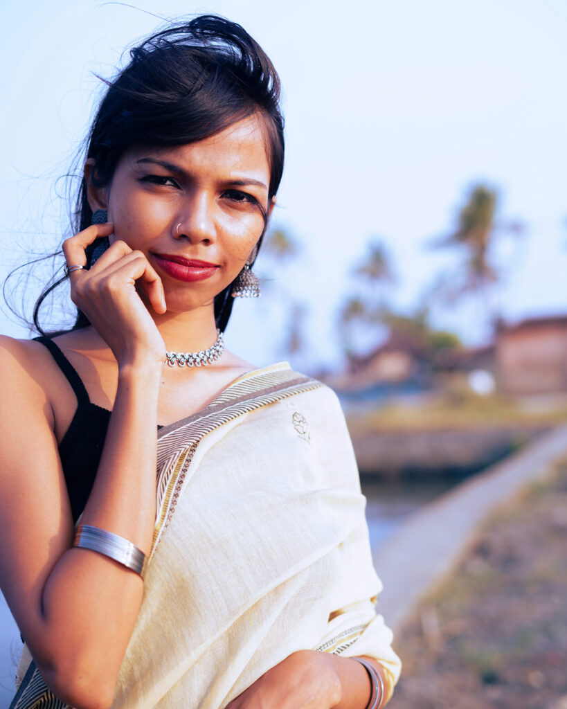 Woman in a cream saree and black blouse by the river, wind in her hair