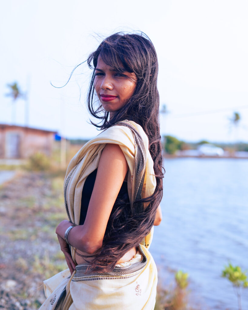 Woman in a cream saree and black blouse by the river, wind in her hair