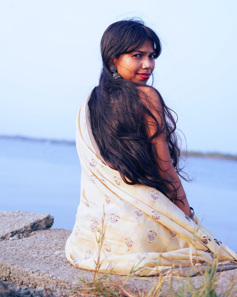 Woman in a cream saree and black blouse by the river, wind in her hair