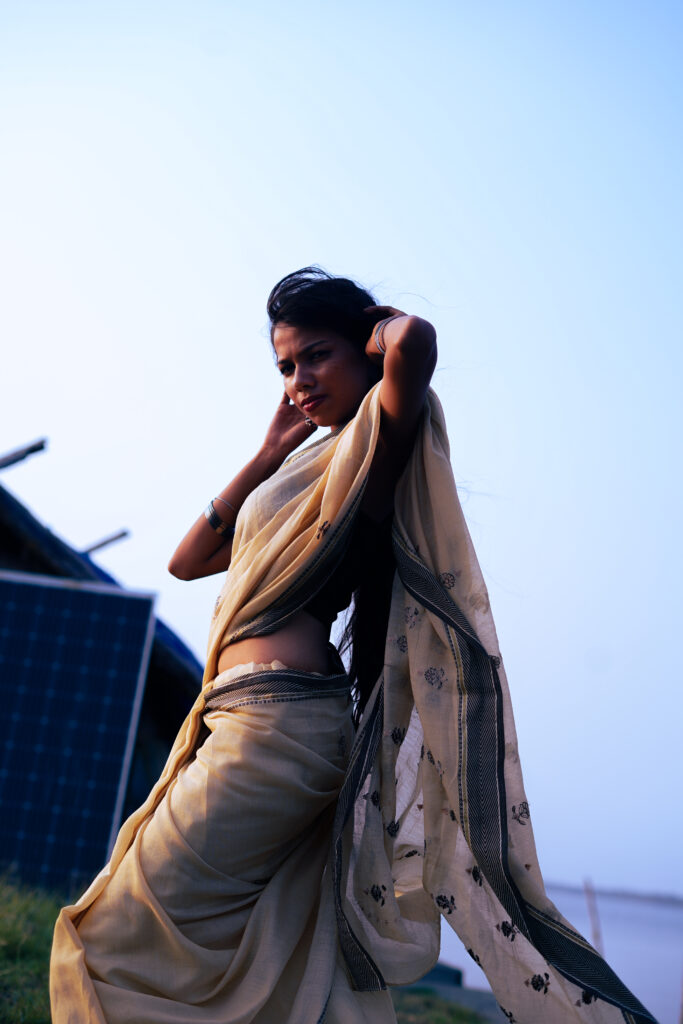 Woman in a cream saree and black blouse by the river, wind in her hair