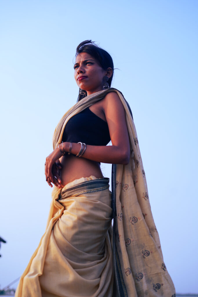 Woman in a cream saree and black blouse by the river, wind in her hair