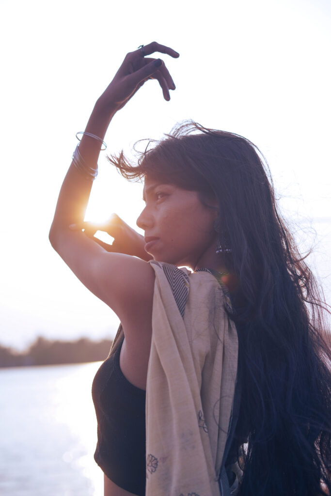 Woman raising one arm against a bright sunset over a river, in silhouette