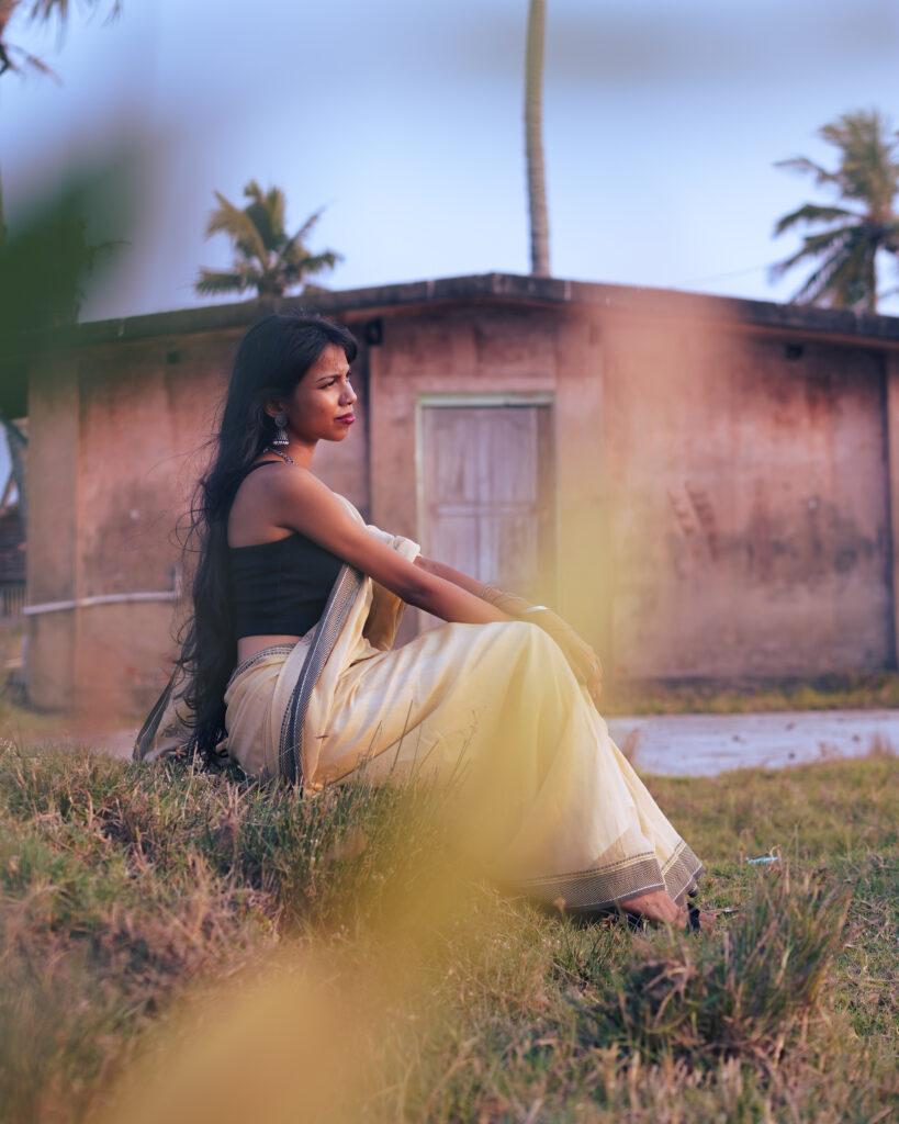Woman in a cream saree and black blouse by the river, wind in her hair