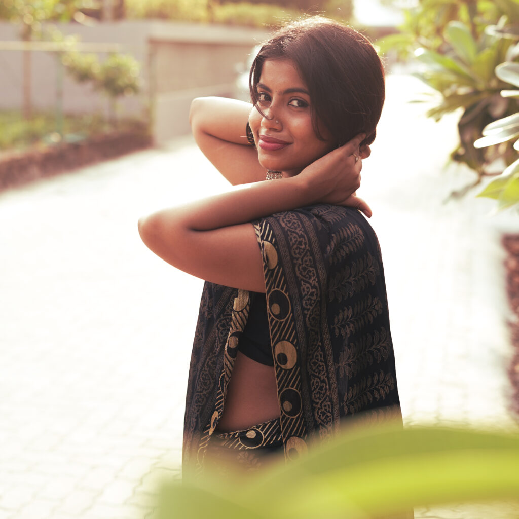 Woman in a black printed saree on a sunlit paved path, saree catching the light