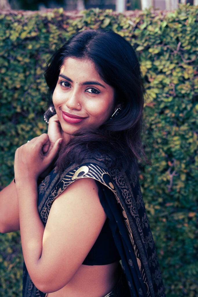 Smiling woman in a black and gold saree against a green wall